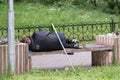 A dirty homeless man sleeping in a black jacket on a street bench.