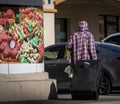 Homeless person pulling suitcase passing a market sign with a photo of various