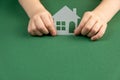 Homeless shelter and real estate concept. Close up of child hands holding white paper house and heart on green background. Royalty Free Stock Photo