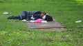 A homeless tramp sleeps on a dirty carpet spread on the grass