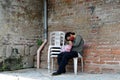 A homeless woman sleeping on a monoblock chair at the side of the brick wall in an old church yard Royalty Free Stock Photo