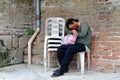 A homeless woman sleeping on a monoblock chair at the side of the brick wall in an old church yard Royalty Free Stock Photo