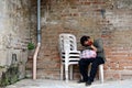 A homeless woman sleeping on a monoblock chair at the side of the brick wall in an old church yard Royalty Free Stock Photo