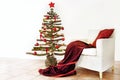 Homemade alternative Christmas tree of rustic raw wood branches decorated with fairy lights and red balls next to an armchair with