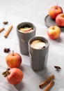 Homemade apple punch with apples and cinnamon in cups on a light background with fresh fruits, spices and shadows