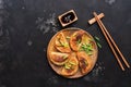 Homemade Asian fried dumplings with chives, soy sauce and chopsticks on a black stone background. Korean Japanese food. Top view,