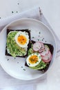 Homemade avocado toasts with soft boiled egg, radish, chives and sesame mix up on white plate and grey cotton napkin