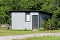 Homemade backyard tool shed storage area made from metal panels with doors and window surrounded with grass gravel and forest