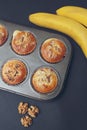 Homemade Banana Chocolate Muffins sprinkled with Nuts in a Baking form in a Black background with Bannana Fruit. Top