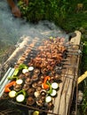 Homemade barbecue on the grill with open fire and smoke. Meat and vegetables with mushrooms and zucchini on wooden sticks.