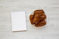 Homemade beef sausage kolache on a white plate, blank notebook on a white wooden background, top view. Space for text