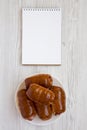 Homemade beef sausage kolache on a white plate, blank notebook on a white wooden surface, top view. Copy space