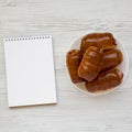 Homemade beef sausage kolache on a white plate, blank notepad on a white wooden surface, top view. Copy space