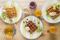 Homemade Belgian waffles with jam, honey, pieces of banana, kiwi fruit, kumquat and cranberries on striped plates.