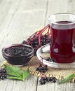 Homemade black elderberry syrup in glass jar and bunches of black elderberry on wooden table