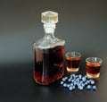 Homemade blueberry liqueur, a strong alcoholic drink in a glass decanter and two glasses on a black background, next to a handful Royalty Free Stock Photo