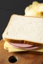Homemade Bologna Cheese Sandwich with Chips on a rustic wooden board on a black background, side view
