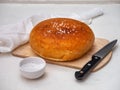 Homemade bread on a wooden unpainted board with coarse salt in a white salt shaker and a kitchen knife, next to it is a white