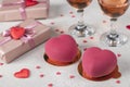 Homemade bright mousse cakes Hearts with pink velvet coating and two glasses of rose wine on light background