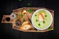 Homemade broccoli cream soup with croutons in white bowl on wooden board.