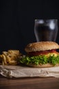 Homemade burger and french fries with oregano and frozen glass a tasty soda. Humburger served on pergament paper and wooden board.