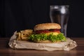 Homemade burger and french fries with oregano and frozen glass a tasty soda. Humburger served on pergament paper and wooden board.