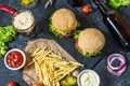 Homemade burgers with beef and fried potatoes and glass of cold dark beer on stone table