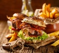 Homemade burgers with grilled bacon, red onion, fresh lettuce, cucumber pickles, tomato and aromatic mayonnaise sauce on a wooden