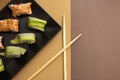 Homemade california and cucumber sushi rolls with sesame seeds on a black square plate on a brown beige background with wooden Royalty Free Stock Photo