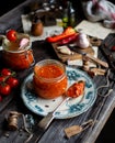 Homemade canned hot tomato sauce adjika in glass jar standing on vintage plate