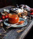 Homemade canned hot tomato sauce adjika in glass jar standing on vintage plate