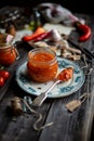 Homemade canned hot tomato sauce adjika in glass jar standing on vintage plate