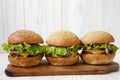 Homemade cheeseburgers on wooden board over white wooden background, side view