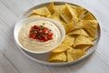 Homemade cheesy dip in a bowl, yellow tortilla chips over white wooden surface, side view. Close-up