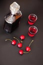 Homemade cherry liqueur in a bottle and two glasses, ripe berries nearby on a black background Royalty Free Stock Photo