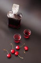 Homemade cherry liqueur, glass bottle and two glasses on a black background, several ripe red berries next to it Royalty Free Stock Photo