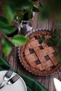 Homemade chocolate berry fruit pie on wooden background with green leaves, summer pie outdoors