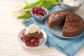 Homemade chocolate cake and bowls with morello cherries and whipped cream, some tulip flowers and a blue napkin on a bright wooden Royalty Free Stock Photo