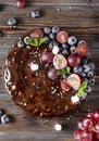 Homemade chocolate cake with fresh berries, red grapes and blueberries, mint, coconut crumbs and marshmallows on a wooden brown Royalty Free Stock Photo