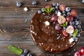 Homemade chocolate cake with fresh berries, red grapes and blueberries, mint, coconut crumbs and marshmallows on a wooden brown Royalty Free Stock Photo