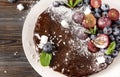 Homemade chocolate cake with fresh berries, red grapes and blueberries, mint, coconut crumbs, powdered sugar  on a white plate on Royalty Free Stock Photo