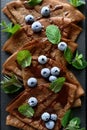 Homemade chocolate crepes served with blueberries, sauce and mint leaves on slate plate. Selective focus. Top view. Copy space Royalty Free Stock Photo