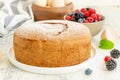 Homemade classic vanilla sponge cake or biscuit sprinkled with powdered sugar and fresh berries on a white plate on a light wooden