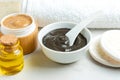 Homemade clay mask for the face and body in a white bowl nect to scrub and oil in bottles. Reusable lufa pads for mask