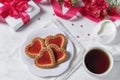 Homemade cookies in the form of hearts with red jam on Valentine`s Day. On a marble table with a gift, tea and roses Royalty Free Stock Photo