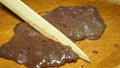 Chef softens raw beef liver and often beats it with a knife, on wooden cutting board.