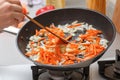 Homemade cooking. A woman fries onions and carrots in a hot frying pan with vegetable oil. Close-up