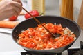 Homemade cooking. A woman fries onions, carrots and tomatoes in a hot pan with vegetable oil. Close-up.