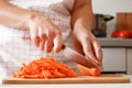 Homemade cooking. Woman in the kitchen cutting a carrot on a cutting wooden board. Healthy fresh food.Close-up