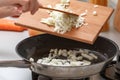 Homemade cooking. A woman with a wooden cutting board adds onions to a hot pan with vegetable oil. Close-up